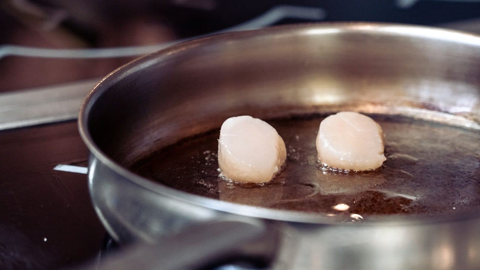 Scallops searing in a stainless steel pan on a hob.