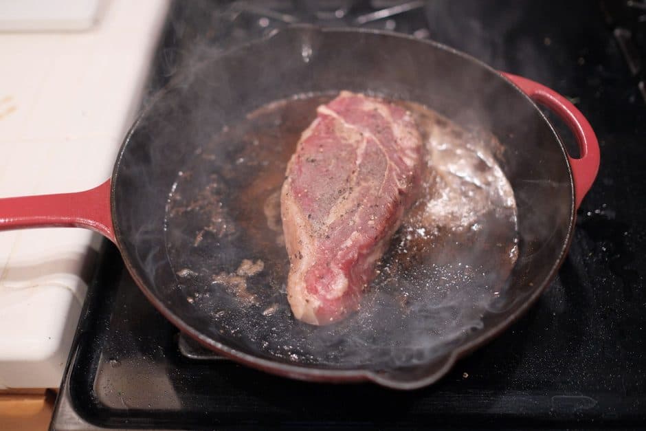 A steak searing in a stainless steel skillet.